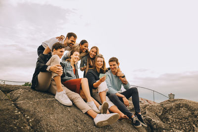 People sitting on rock against sky