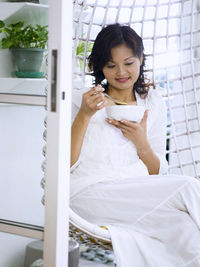 Woman having food while sitting in swing chair at home