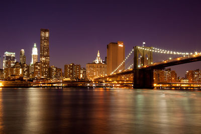 Illuminated bridge over river with buildings in background at night