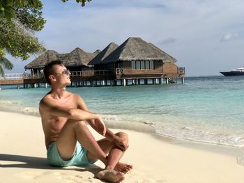 Man sitting on swimming pool at beach against sky