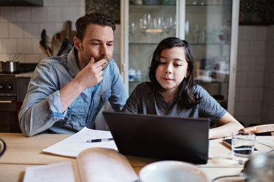 Serious father and studious son looking at laptop on table