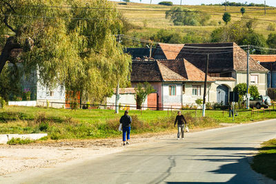 Rear view of people walking on road by building