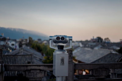 Close-up of coin-operated binoculars against buildings in city during sunset