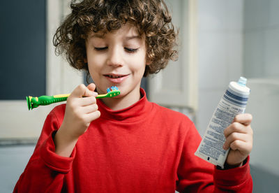 Boy holding toothbrush while standing in bathroom at home