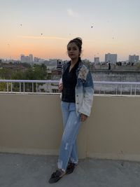 Portrait of beautiful young woman standing against cityscape at sunset