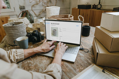 Hands of craftswoman using laptop on workbench