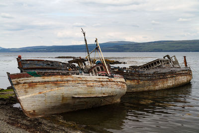 Abandoned boat moored at sea shore against sky