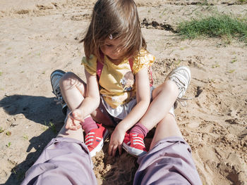 Toddler girl wearing red sneakers sitting at the beach 