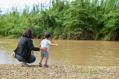 A mother watching over her child stands watching the river on the beach.