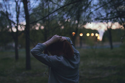 Woman tying hair while walking on field against trees