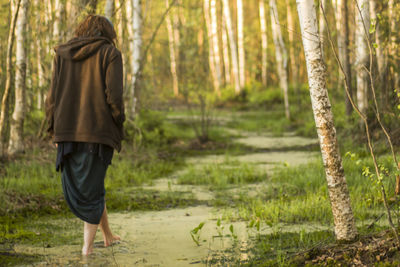 Rear view of woman walking in swamp against trees at forest