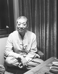 Portrait of smiling senior man sitting on chair against curtains at home