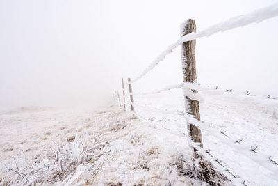 Wooden post on snow covered field against sky