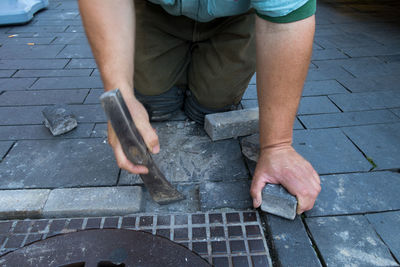 Midsection of construction worker working with axe by manhole on footpath