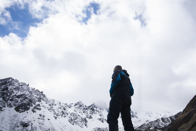 Low angle view of man standing on snowcapped mountain against cloudy sky