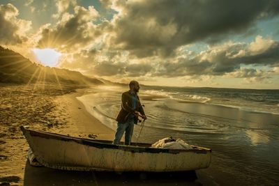Man holding anchor while standing in abandoned boat at beach during sunset