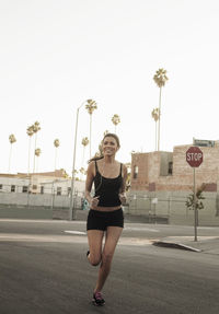 Happy young woman listening music while jogging on street during sunset