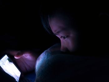 Close-up of boy using mobile phone against black background