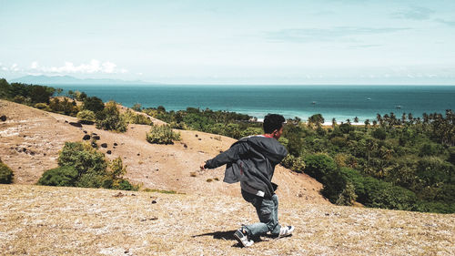 Full length of happy man running on field with sea in background