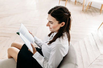 High angle view of woman reading book sitting on sofa