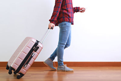 Low section of person walking with suitcase against white wall