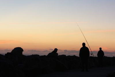Silhouette people sitting by sea against clear sky during sunset