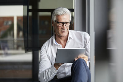Serene businessman sitting on ground in office, using digital tablet