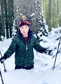 Boy standing in the snow with a tree in the background.