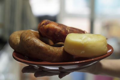 Hand holding a plate with soft cheese and portuguese sausages