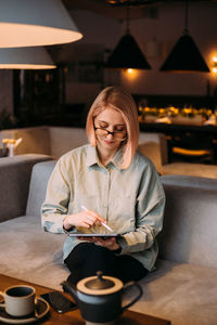 Woman holding coffee while sitting on table at restaurant