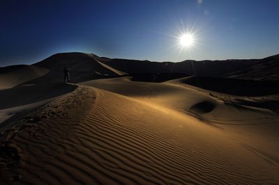Person walking on sand dune in desert against sky