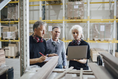 Female worker showing laptop to colleagues while standing by rack in industry