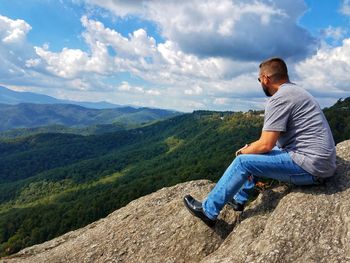 Man sitting on mountain against sky