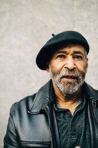 Portrait of man wearing hat standing against wall