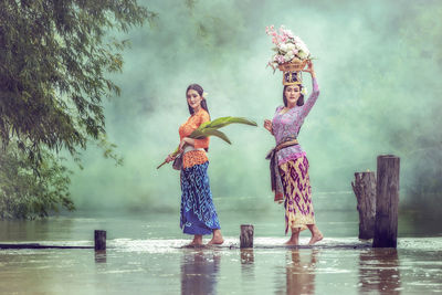 Full length of friends carrying flowers while standing by lake