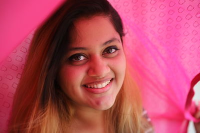 Portrait of smiling young woman under pink fabric