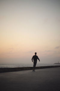 Rear view of woman walking on beach against sky during sunset