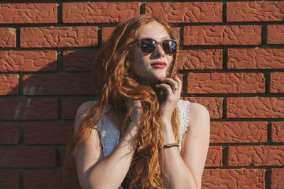 Portrait of a young redhead woman leaning against brick wall