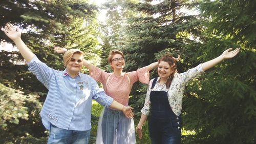 Happy friends with arms outstretched standing amidst trees