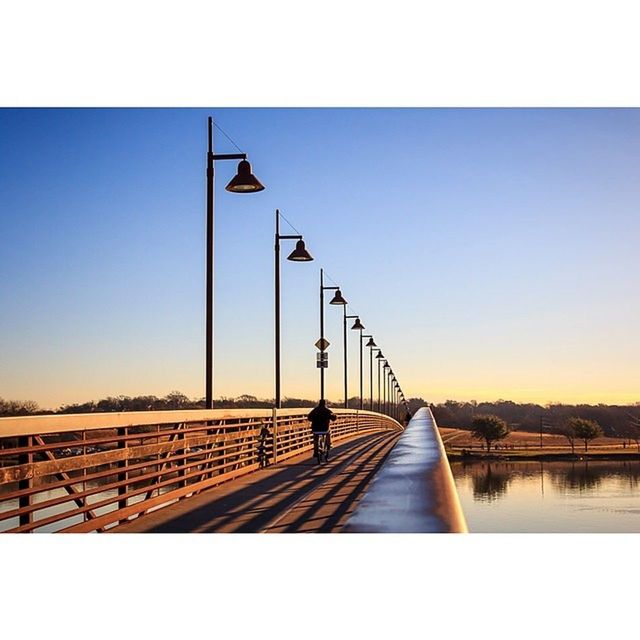 clear sky, transfer print, copy space, built structure, water, connection, architecture, bird, auto post production filter, bridge - man made structure, railing, river, bridge, sky, sunset, street light, transportation, outdoors, pier, nature