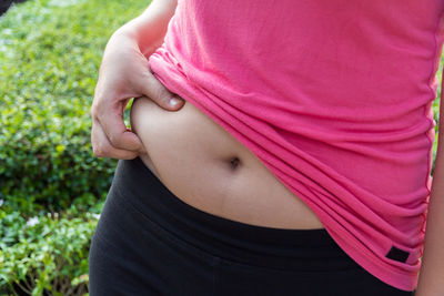 Midsection of woman pinching abdomen in yard