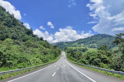 Empty road along trees and plants against sky