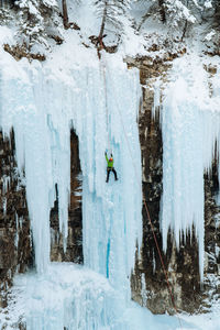 Verticle view of ice climber scaling frozen waterfall on cliff in canada during winter.