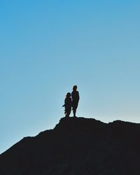 Silhouette of people standing on mountain against blue sky