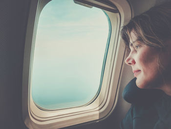 Beautiful girl looks out the window of the airplane. summer vacation, travel, melancholy concept.