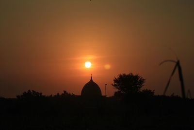 Silhouette temple against building during sunset