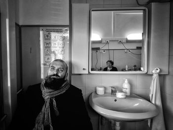 Matured man sitting in bathroom while woman reflecting in mirror