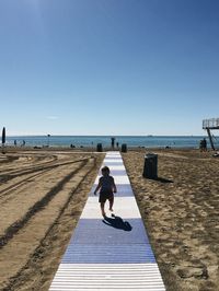 Rear view of man walking on beach against clear sky