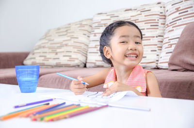 Close-up of girl drawing at table against sofa