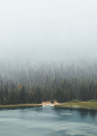 Calm lake with misty trees against the sky